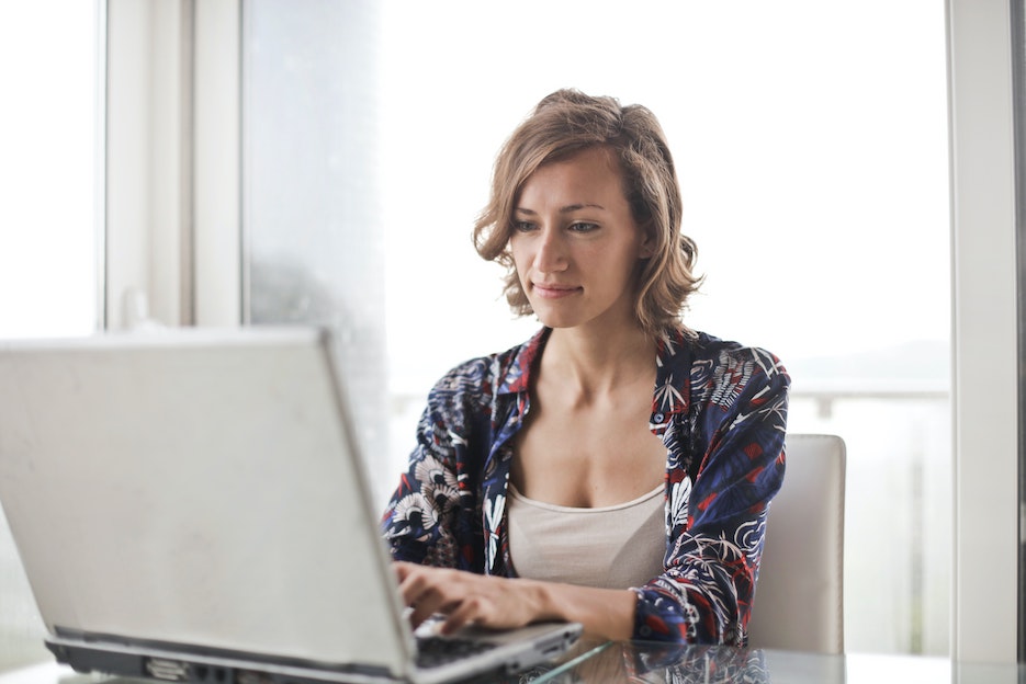 Eine junge Frau, die am Schreibtisch sitzt, lächelt und auf ihr Laptop schaut.