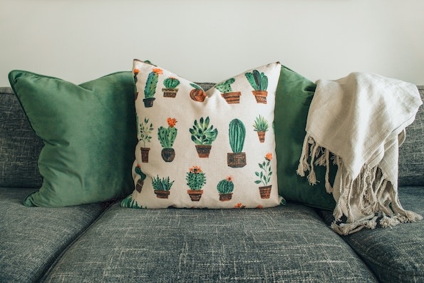 graue Couch mit grünen Kissen und einer weißen Decke.