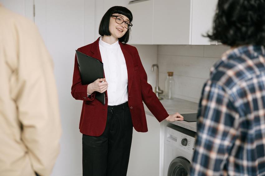 Frau mit rotem Blazer und einem Ordner in der Hand, steht vor einer Küchenzeile.